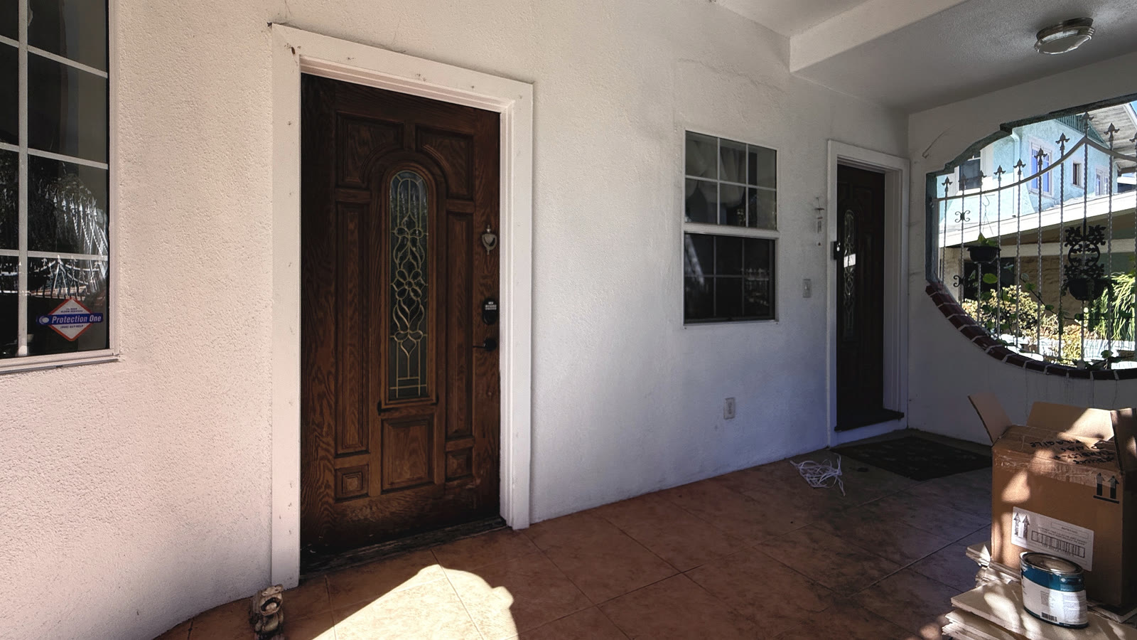 Covered entry porch with white stucco walls and a terracotta-colored tile floor, a dark front door with an arched decorative-glass insert, and a window beside it.