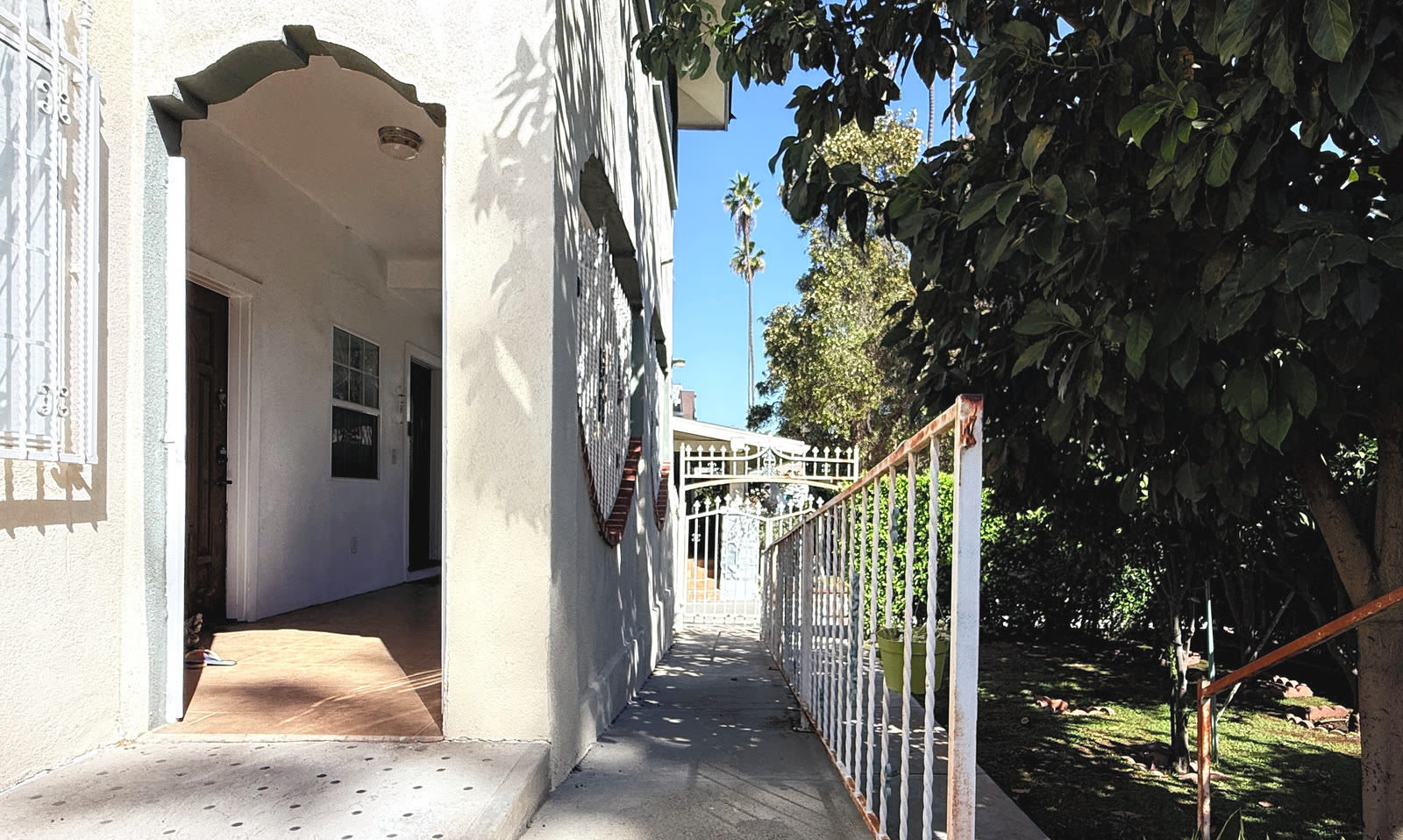 The concrete entry walk beside the house, with an arched stucco opening at left framing the covered porch and the white railing and street gate at right.