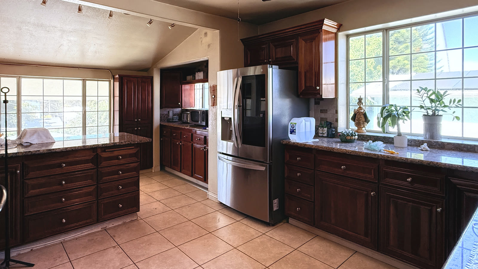 The kitchen seen wide: dark cabinets, a peninsula with drawers, granite counters, large grid windows on two sides and tile flooring.