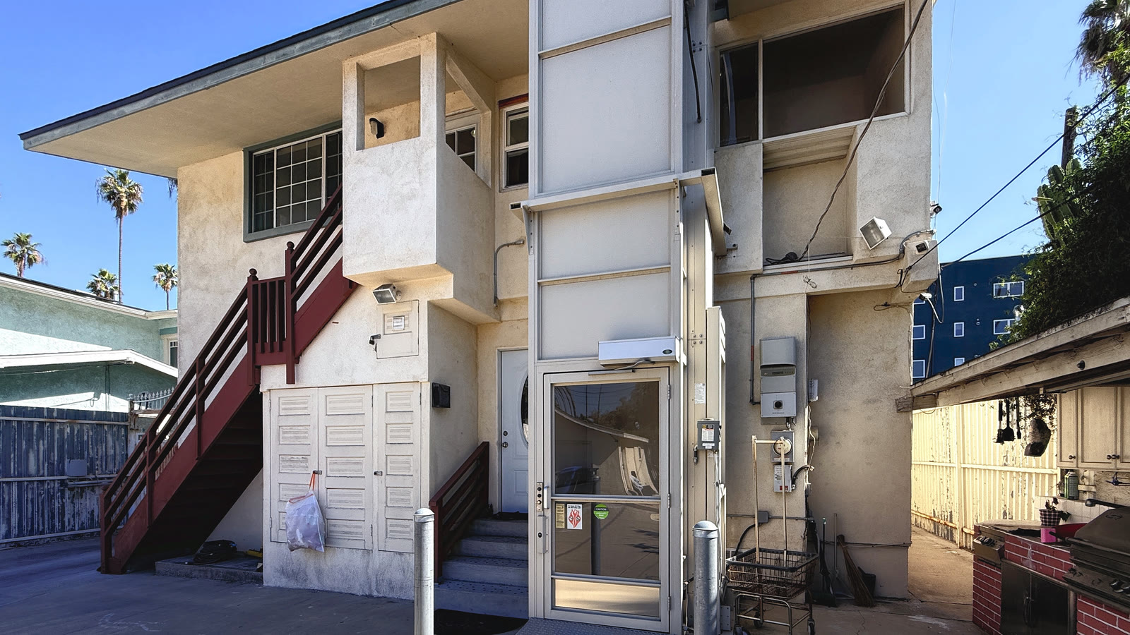 The ground-level lift enclosure in the rear court, a tall paneled tower with a glass door, beside the exterior stair.