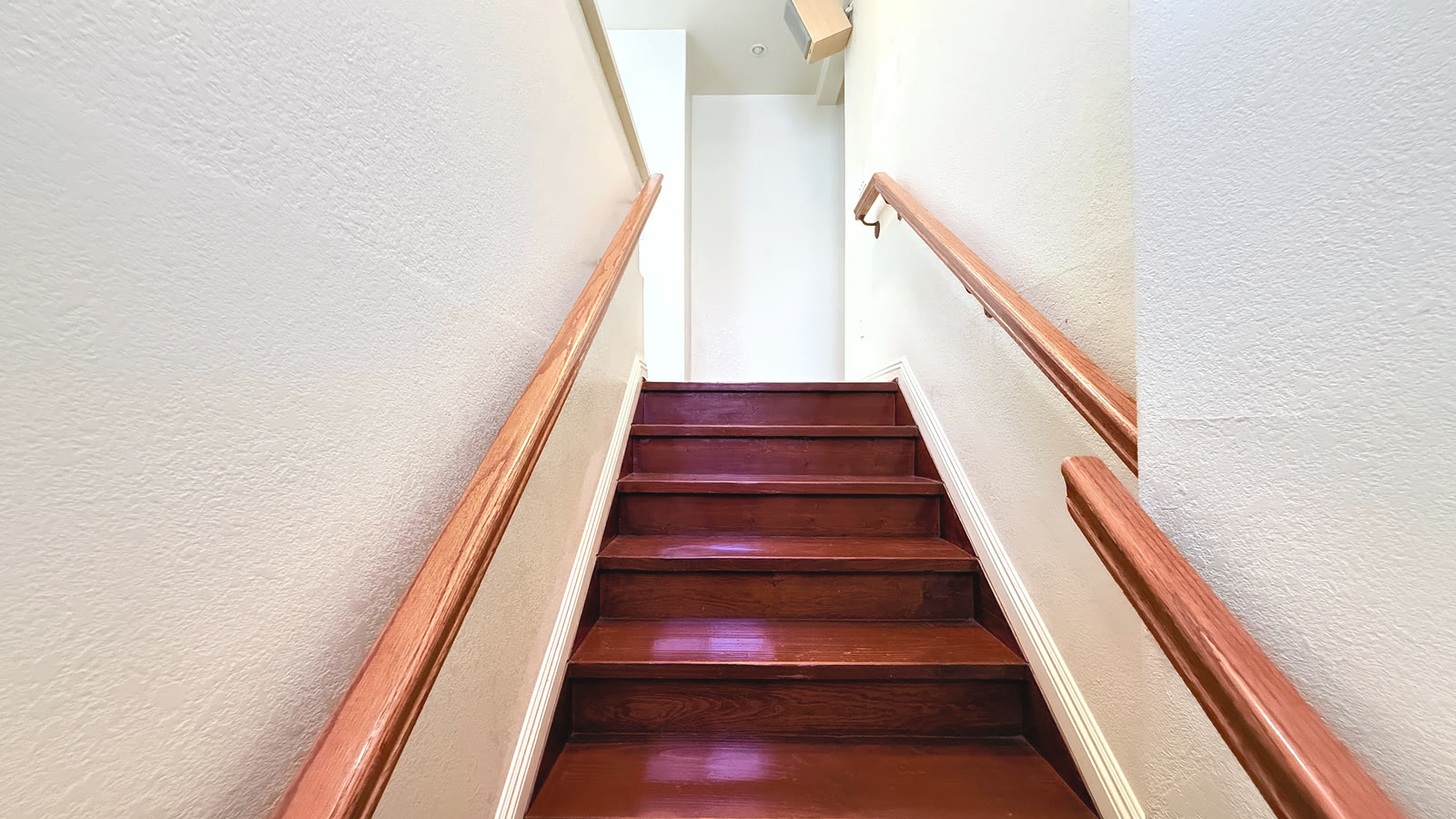 The interior front stair seen from the bottom, with stained treads and handrails on both walls.